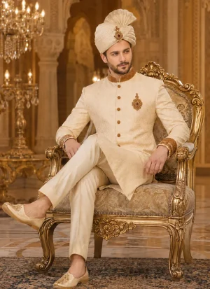 Groom seated in a cream and gold sherwani with matching turban and khussa