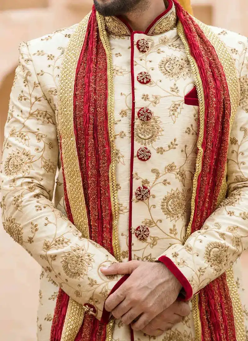 Close-up of an ivory sherwani with fine gold embroidery and deep red trim