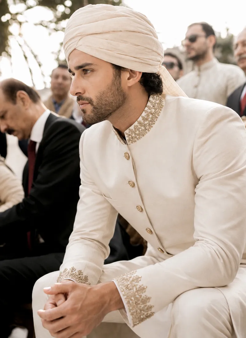 Close view of hand-embroidered gold zari on a white sherwani stand collar