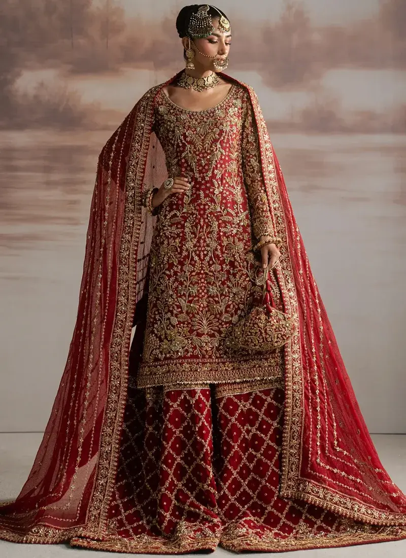 Deep Red Nikkah Sharara Suit with Gold Diamond Jaal Deep red bridal ensemble front view beneath a sheer veil with ornate gold floral arch embroidery