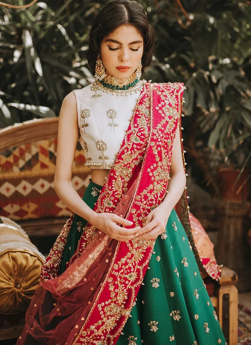 Emerald green mehndi lehenga choli seated front view with floral hem and rose pink dupatta