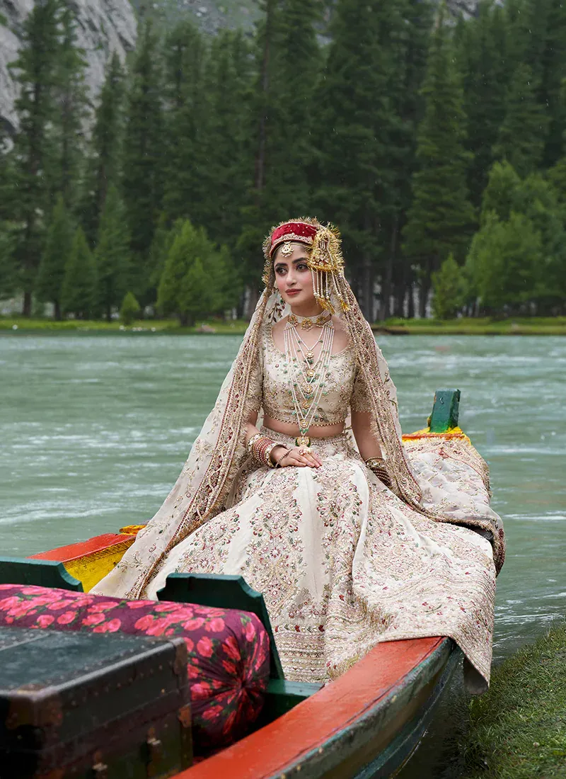 Seated view of the lehenga spread out wide, with the short-sleeved ivory choli and organza dupatta draped over the head