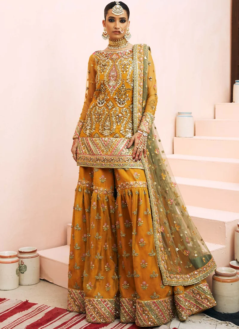 Mustard Mehndi Gharara Suit with Pink Chevron Borders Mustard mehndi gharara suit seated close-up with gold and pink bodice embroidery and olive dupatta border