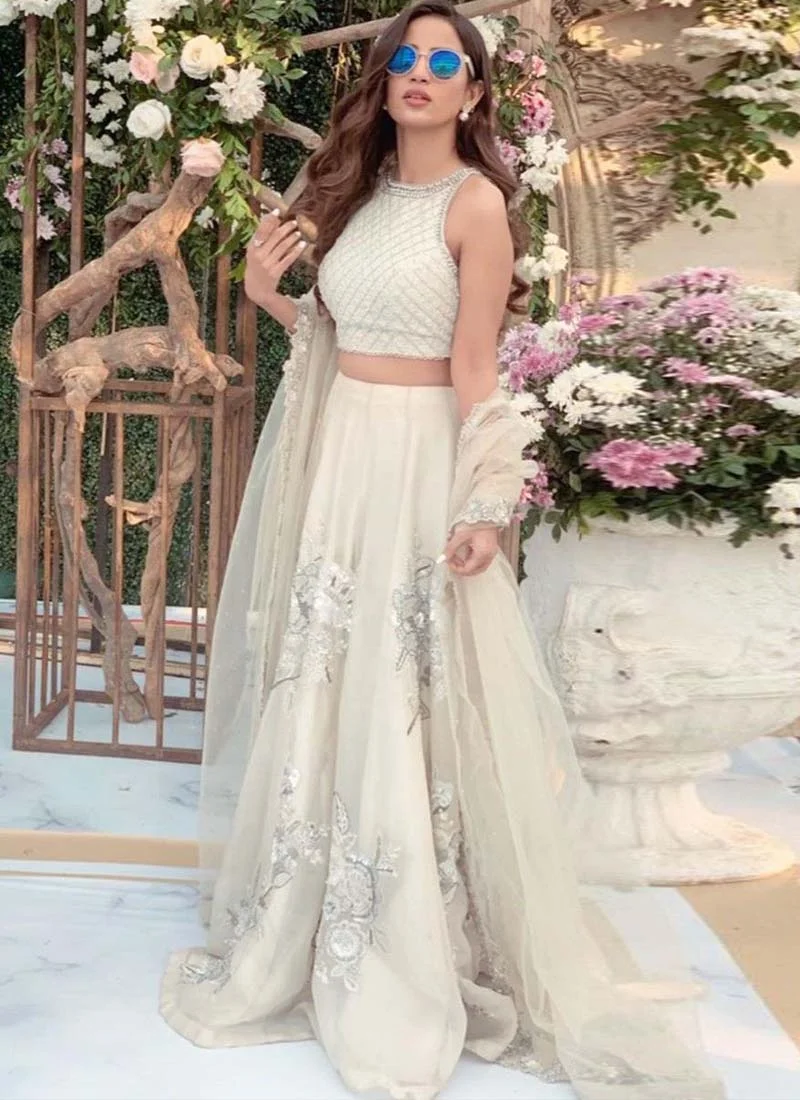 White Engagement Lehenga Choli with Diamond Lattice Bodice White lehenga choli, seated front view with silver floral motifs and a diamond-lattice sleeveless blouse.
